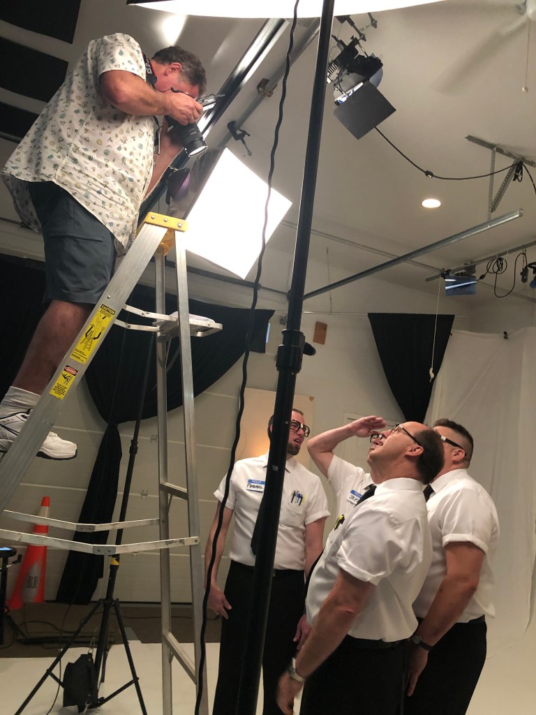 Photographer on ladder shooting 4 men on a photo set of a studio